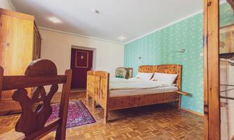 A cozy bedroom with wooden furniture and a double bed. The walls are designed in a light green color and the floor is laid with parquet.