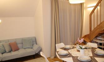 A cozy living room with a blue sofa and a white dining table. The room is well-lit and has an inviting atmosphere.