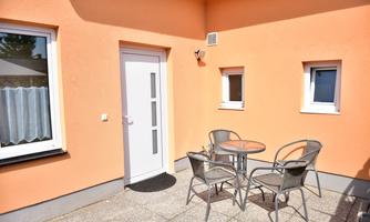 A cozy outdoor area with a table and four chairs. The walls are painted in a warm orange, and the windows are bright.