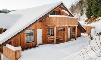 A charming wooden house in winter, surrounded by fresh, white snow. The sloping roof and large windows give the building a cozy atmosphere.