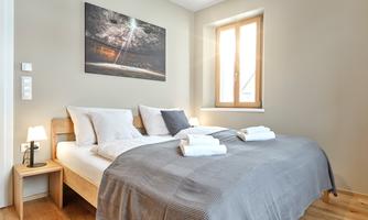 A modern bedroom with a double bed and fresh towels. Daylight comes through the window and a decorative picture hangs on the wall.