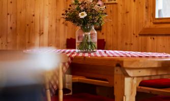 A cozy wooden room with a table and chairs. On the table, there is a vase with fresh flowers.