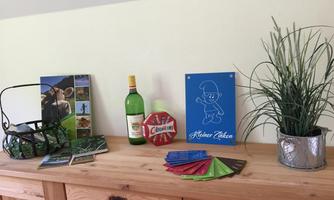 A wooden table with various items, including a wine bottle, a plant, and several brochures. On the table, there is also a colorful sign that reads "Little Dancer."
