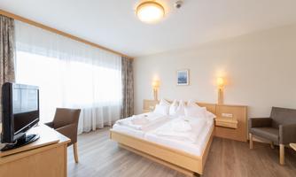 A modern hotel room with two beds and a television. Large windows provide plenty of daylight.