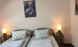 A cozy bedroom with two single beds, striped blankets and pillows. A colorful piece of artwork hangs on the wall, and there are nightstands with lamps.