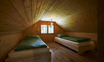 A cozy room in the attic with two single beds and wooden paneling. Soft light shines in through the window.