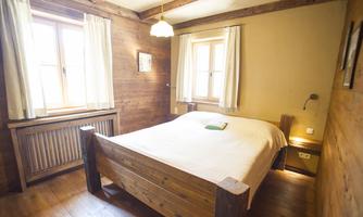 A cozy bedroom with a wooden bed and warm, rustic walls. Bright windows and curtains create an inviting atmosphere.