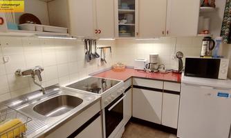 A modern kitchen with bright cabinets and a red workspace. It includes a sink, cooking facility, microwave, and refrigerator.