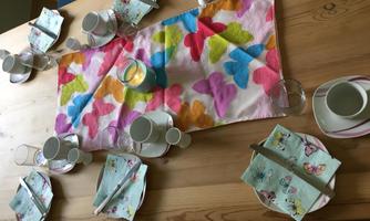 A table beautifully set with colorful napkins and plates. In the middle lies a tablecloth with butterflies.