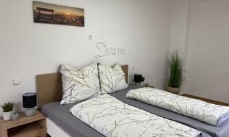 A cozy bedroom with two beds and modern decor. The walls are light, and there are plants as well as an inspiring wall graphic.