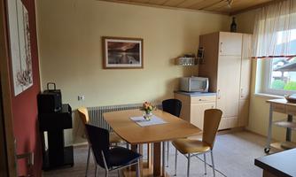 A simple kitchen with a table and four chairs. There is a microwave, a refrigerator, and some decorative elements on the walls.