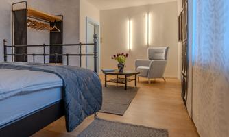 A modern bedroom with a cozy bed and an armchair. There is a small table and fresh flowers on the table.