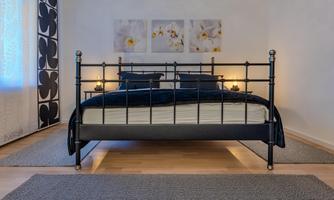 A cozy bedroom with a metal bed and two nightstands. Pictures of flowers hang on the wall and there is a bright rug on the floor.