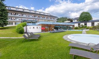 A beautiful hotel with a well-maintained garden and loungers. In the foreground, there is a pool, and in the background, you can see the mountains.
