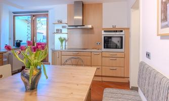 A modern kitchen with wooden cabinets and a large window front. On the table, there is a vase with colorful tulips.