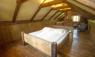 A cozy bedroom in the attic with a large wooden bed. The walls are made of wood, and there is a small seating area.