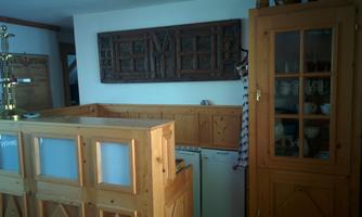 A cozy kitchen with wooden paneling and a decorative wall panel. Dishes and cups are visible in the cabinet.