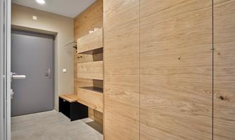 A modern hallway with light wood and a gray door. On the wall, there are shelves and a bench for sitting.