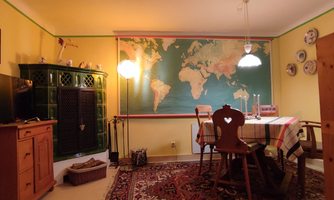 A cozy dining area with a large world map on the wall. The room is brightly lit and has a rustic decor with a table and chairs.