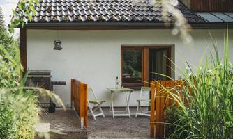 A cozy outdoor area with a small table and chairs in front of a house.  
Surrounded by greenery and a tranquil atmosphere.