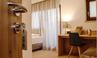 A modern room with a desk and a comfortable bed. Bright curtains let in a lot of light.
