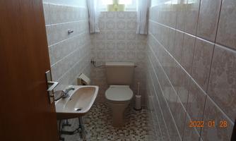 A simple bathroom with a toilet and a sink. The walls are brightly tiled, and the window lets in daylight.