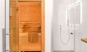 A modern bathroom with a wooden sauna on the left side and a glass shower on the right side. The sauna is equipped with towels and a small bucket.