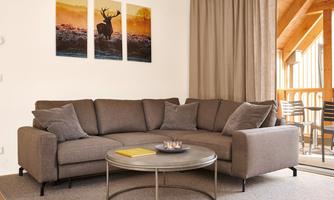 A cozy living room with a brown sofa and a round table. On the wall hang pictures of a deer in a natural setting.