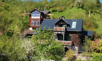 A charming wooden house surrounded by green hills and trees. The architecture is appealing and blends well into the nature.