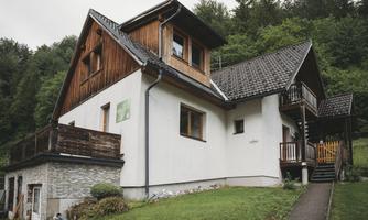 A charming house with wooden cladding and a large garden. It is surrounded by green trees and has an inviting entrance.