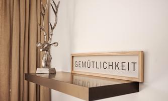 <p>An elegant wall decoration with the word "Gemütlichkeit" in a wooden frame. Next to the frame stands a stylish sculpture of a deer.</p>