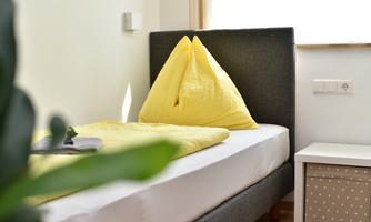A simple bedroom with a bed and yellow pillows. Next to the bed is a nightstand with a decorative container.