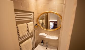 A modern bathroom with a large mirror and a towel warmer. The walls are covered with light tiles, and there are toiletries placed on a shelf.