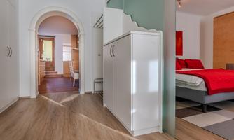 A modernly furnished room with a flowing transition to a bedroom. The floor is made of light wood and the furniture is simple and elegant.