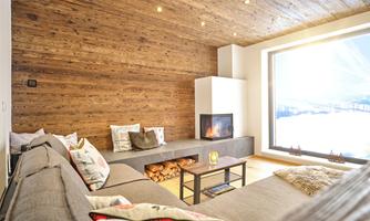 A modern living room with a cozy couch and a fireplace. Large windows offer a view of a snowy landscape.