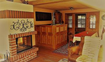 A cozy living space with an open fireplace and wooden furniture. Large windows provide plenty of light and a warm atmosphere.