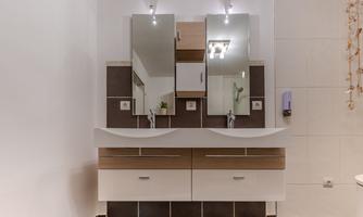 A modern bathroom with an elegant sink and large mirrors. The walls are light and the furniture is designed in neutral colors.