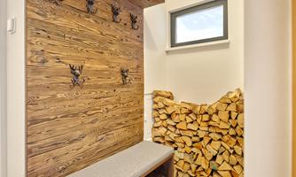 An elegant entrance area with a rustic wooden wall and hooks in antler shape. On the left, a stack of firewood can be seen.
