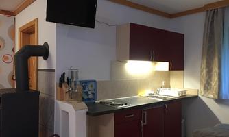 A modern kitchen unit with a red cabinet and a sink. There is a television on the wall and next to the kitchen is a fireplace.