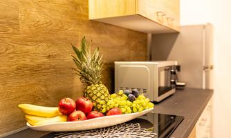 A modern kitchen area with fresh fruit on a white plate. In the background, a microwave and a refrigerator are visible.
