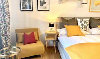 A stylish bedroom with a comfortable bed and a cozy armchair. The walls are adorned with pictures, and the decor is in warm colors.
