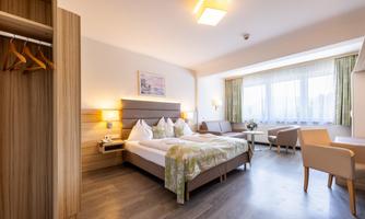 A modern hotel room with a large bed and cozy furniture. The windows provide plenty of daylight and a beautiful view.