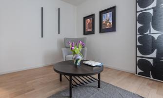 A cozy room with a comfortable armchair and a round table. On the table is a vase with flowers and a book.