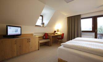 A modern hotel room with two beds and a desk. The room is bright and friendly, with a window and a television.
