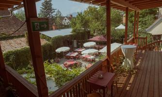 A cozy outdoor area of a restaurant with red tables and umbrellas. The area is surrounded by green plants and invites you to linger.