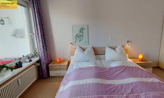 A cozy bedroom with a double bed and white pillows. Natural light floods in through the window, and there are a variety of decorative elements on the nightstands.