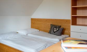 A cozy bedroom with a double bed and a wooden frame. On the bed, there is a pillow with a heart on it.