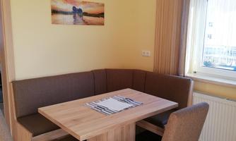 A cozy dining corner with a wooden bench and chairs. The walls are painted in soft colors, and a picture decorates the room.