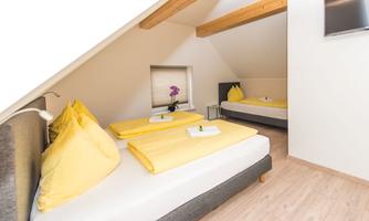 A cozy room with two beds and yellow blankets. The walls are bright, and the wooden beams create a friendly atmosphere.