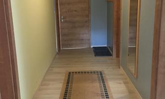 A bright hallway with a wooden door and a large mirror. The floor is made of light wood and a carpet adds coziness to the room.